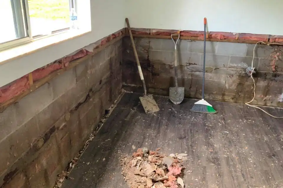 Lovell Basement Solutions, LLC shovels and broom propped against wall of the basement with bad water damage- Edwardsville, IL